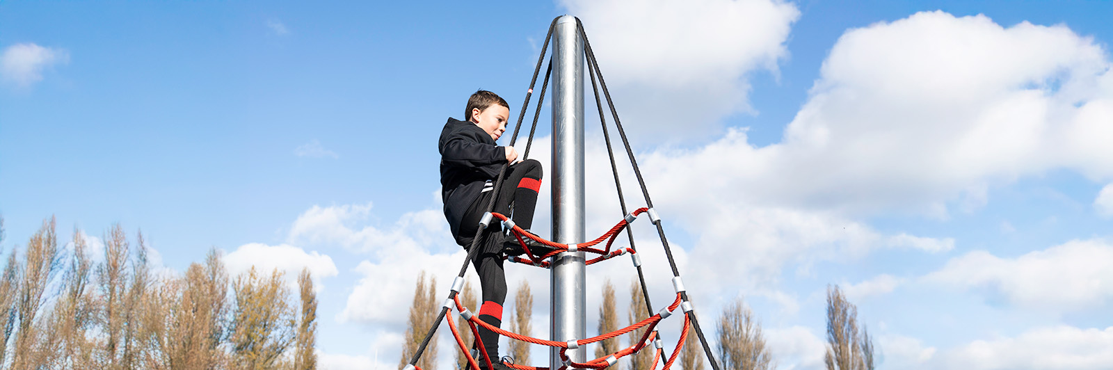 Boy climbing up a climbing net. He is almost at the top.